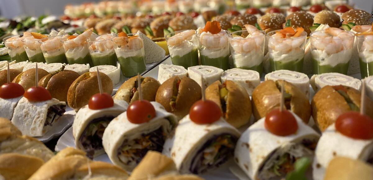 Grand buffet dressé : sandwichs triangles, verrines, wraps et mini-burgers alignés sur plusieurs rangées
